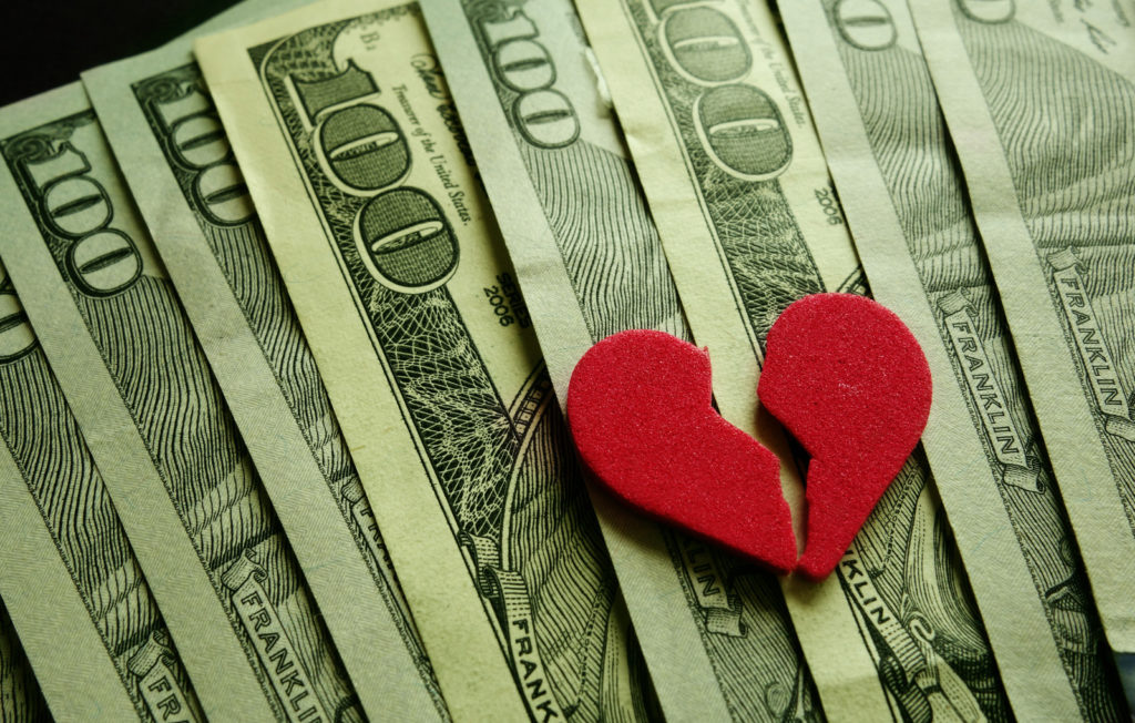 Shows a split, broken red heart laying on top of money