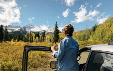 Woman standing next to open car door facing view of mountains and holding a camera