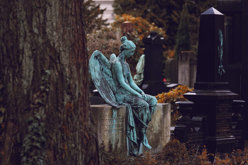 Very old and sad-looking angel statue sitting on family gravestones in cemetery