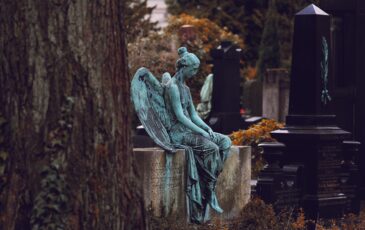 Very old and sad-looking angel statue sitting on family gravestones in cemetery