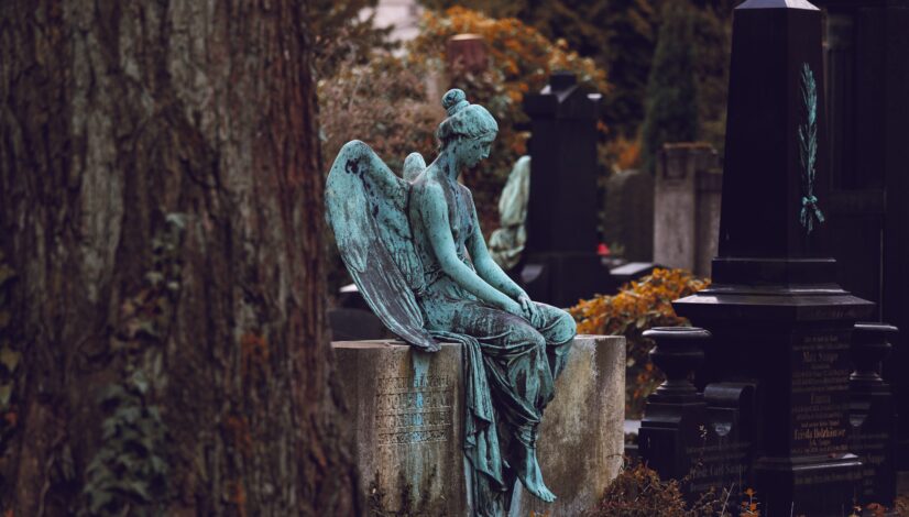 Very old and sad-looking angel statue sitting on family gravestones in cemetery